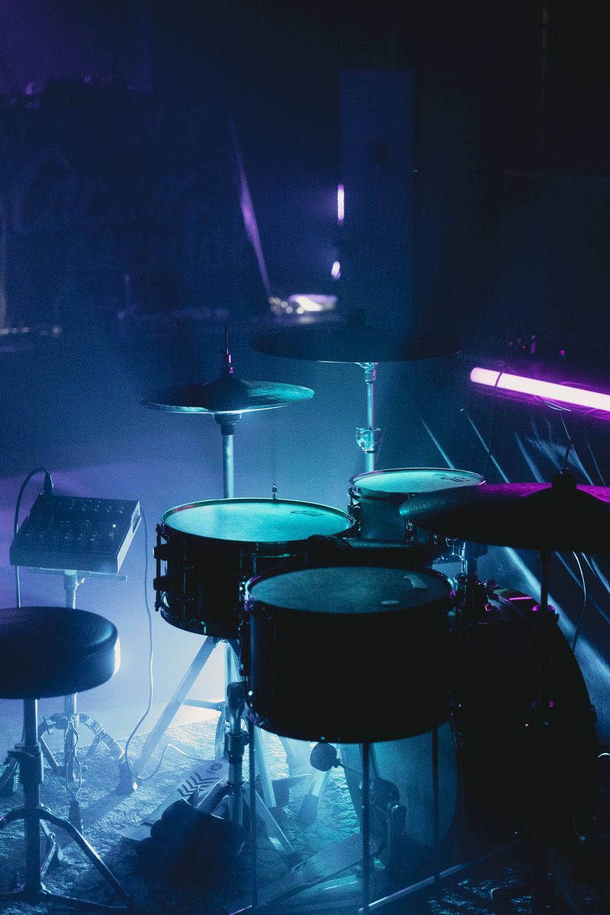 Dimly lit drum set on stage with concert lighting, creating a moody ambiance.